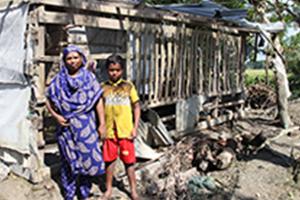 Two people stand outside their home, ruined by Cyclone Bulbul